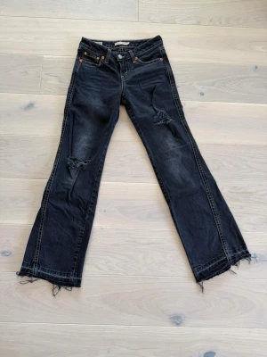 Svarta Levi's jeans med slitningar - Säljer ett par svarta Levi's jeans med raka ben och fransiga benslut. Jeansen har slitningar (menade) på låren och klassiska fem fickor. Perfekt för dig som gillar en avslappnad och trendig stil. Dessa jeans finns inte att få tag på längre🔥❤️