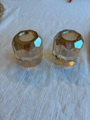 Bruna facettslipade ljushållare i glas - Två stycken bruna ljushållare i glas med facettslipad design. De har en cylinderformad kropp och reflekterar ljuset snyggt tack vare de många slipade kanterna. Perfekta som dekoration på bordet eller i fönstret.