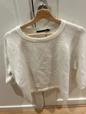 Vit stickad tröja med rund hals - Mysig vit stickad tröja med avslappnad passform och rund halsringning. Tröjan har långa ärmar och ribbade muddar vid halsen och nederkanten. 