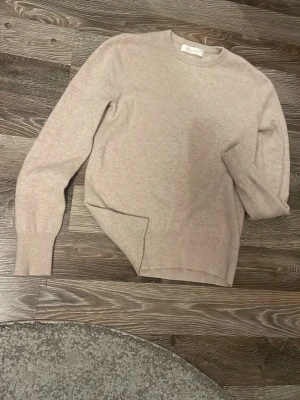 Beige kashmire tröja från Sayless - En klassisk beige stickad tröja från sayless i mjuk kashmir. Tröjan har rund halsringning, långa ärmar och ribbade muddar vid ärmslut och nederkant. Perfekt för lager-på-lager och enkel att matcha med olika outfits.