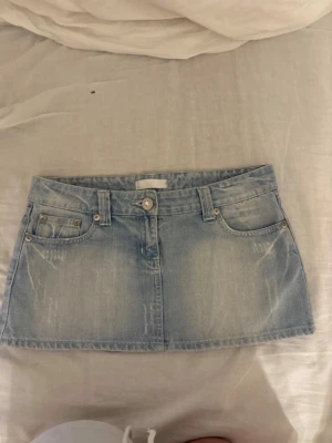 Ljusblå denim minikjol - Ljusblå denim minikjol med klassiska femficksdetaljer och bälteshällor. Kjolen har knapp och dragkedja framtill samt snygga slitningar och tvättade effekter. Perfekt för dig som gillar en avslappnad och trendig look.