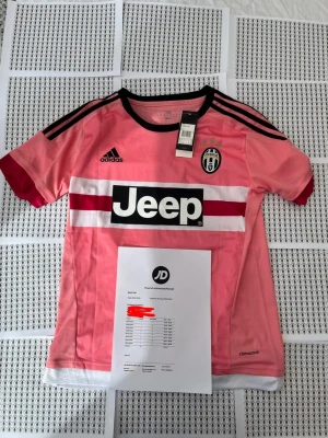 Juventus rosa Pogba matchtröja - Juventus rosa matchtröja från Adidas med Pogba och nummer 10 på ryggen. Tröjan har svarta detaljer, klubbmärke, Jeep-logga på bröstet och climalite-material för bra ventilation. Korta ärmar och sportig passform, perfekt för fotbollsträning eller support.