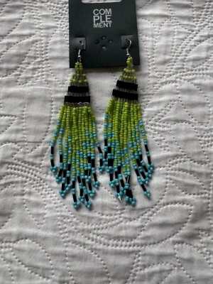 Nya. Färgglada pärlörhängen från Indiska - Säljer ett par långa örhängen  med pärlor i limegrönt, turkost och svart. Örhängena har en fransig design med små glaspärlor i olika färger och svarta stavpärlor som ger en cool kontrast. Perfekta för att ge din look en färgklick!