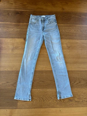 Ljusgrå raka jeans med slits - Snygga ljusgrå jeans med raka ben och slitsar nertill. Klassisk femficksmodell med hög midja och dragkedja. Jeansen har en avslappnad vibe och är gjorda i denim. Mid waisted bootcut 