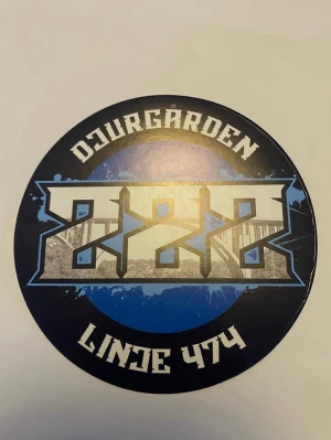 Djurgården klistermärke sofialäktaren  - Runt klistermärke med Djurgården-tema, blå och svart bakgrund med vit och grå grafisk text och motiv. Texten 'Djurgården' och 'Linde 474' syns tydligt. Perfekt för att dekorera personliga tillhörigheter.
