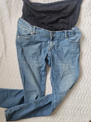 Blå mammajeans från Dr Denim - Säljer ett par ljusblå mammajeans från Dr Denim med mjuk svart mudd över magen. Jeansen har klassisk femficksdesign, smal passform och stretchigt denimtyg. Perfekta för dig som vill ha bekväma och snygga jeans under graviditeten.