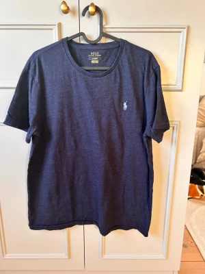 Mörkblå t-shirt från Polo Ralph Lauren - Snygg mörkblå t-shirt från Polo Ralph Lauren med klassisk rund halsringning och den ikoniska broderade loggan på bröstet. Tillverkad i mjuk bomull för en bekväm känsla. Perfekt till jeans eller shorts för en clean look. (M)