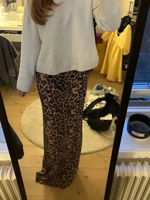 Lång leopardmönstrad kjol - Säljer en lång kjol med leopardmönster i bruna och svarta toner. Kjolen har en rak och smal passform som sitter snyggt över höfterna och faller rakt ner. Perfekt för dig som vill sticka ut med ett djurmönster. Materialet känns mjukt och är ganska genomskinligt.