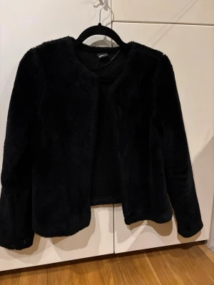 Svart pälsjacka - Snygg svart pälsjacka med rund halsringning och rak passform. Jackan har långa ärmar. Perfekt för att höja din outfit med en lyxig känsla. Är från Gina tricot