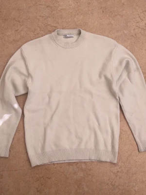 Beige stickad tröja från Zara - Klassisk beige stickad tröja från Zara med rund halsringning och ribbade muddar vid ärmslut och nederkant. Tröjan har en enkel och stilren design som passar till det mesta. Materialet är mjukt och bekvämt.