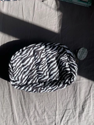 Zebramönstrad necessär med dragkedja - Snygg zebramönstrad necessär i svart och vitt med quiltad utsida och guldfärgad dragkedja. Perfekt för smink eller småprylar. Insidan är vit och lätt att torka av. Praktisk och trendig accessoar för väskan.