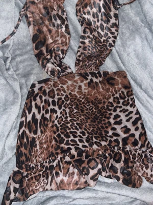 Leopardmönstrad kort klänning - Säljer en leopardmönstrad kort klänning med volangkant nedtill och knytband vid axlarna.