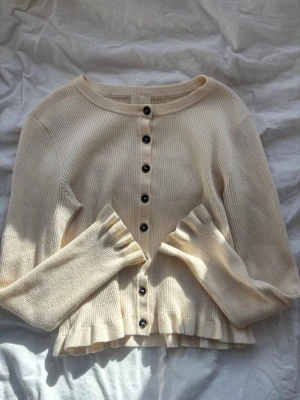 Ribbad tröja med volang - Söt ribbad tröja med svarta knappar framtill och volang. Från HM i storlek S. Super bra skick!