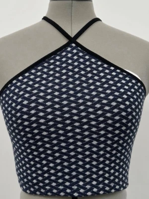 Mörkblå mönstrad halterneck topp - Snygg mörkblå halterneck topp med vitt geometriskt mönster och svarta kanter. Toppen har smala axelband som korsas framtill och ger en trendig look. Perfekt till jeans eller kjol för en cool och modern stil.