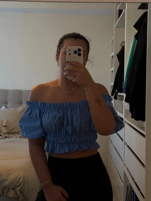 Blå offshoulder croppad topp - Säljer en blå offshoulder topp med croppad passform och resår vid axlar och midja. Toppen har volangdetaljer och är ärmlös, perfekt för en trendig och avslappnad look. Materialet känns lätt och luftigt.