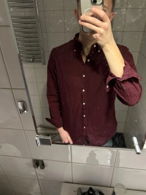 Mörkröd skjorta med knappar - Snygg mörkröd skjorta med klassisk krage och knäppning framtill från Ralph Lauren. Skjortan har långa ärmar och en avslappnad passform. Perfekt för dig som vill ha en stilren look med lite färg.