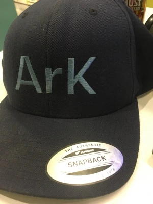Mörkblå snapback keps Ark - Snygg mörkblå snapback keps från Yupoong med broderad text 'ArK' framtill i ljusblått. Klassisk rak skärm och justerbar baksida för perfekt passform. Kepsen har en modern streetwear-look och är tillverkad i ett tåligt tyg.    Jag samlar på kepsar, så de är sparsamt använda och alla har kvar stuket från när de var nya. När jag skickar en keps så gör jag det med mycket vaddering och alltid i en hård kartong. ( är nog ensam om för begagnade kepsar. 