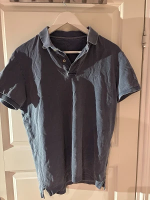 Blå pikétröja från Gant - Klassisk blå pikétröja från Gant med korta ärmar och krage. Tröjan har två knappar vid halsen och diskret Gant-logga broderad på bröstet. Perfekt till jeans eller shorts för en avslappnad men snygg stil.