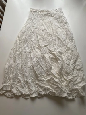 Vit långkjol i bomull med spetsdetaljer - Säljer en vit långkjol i bomull med fina spetsdetaljer. Kjolen har en lätt utsvängd form och resår i midjan för skön passform. Perfekt för sommarens alla tillfällen och enkel att matcha med olika toppar.