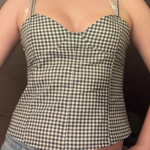 Rutig korsett-topp med smala axelband - Supersöt korsett-topp med smala axelband och rutigt mönster i blått och vitt. Handsydd och köpt i Frankrike i somras. Säljer då jag inte får användning av den. Den har inga defekter. Dragkedja vid sidan. Fråga om fler bilder eller mått! Öppen för prisförslag!