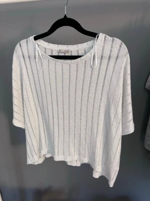 Vit randig croppad topp  - Luftig vit croppad topp från Zara med vertikala ränder och korta ärmar. Toppen har en lös passform, rund halsringning och tunna knytband på axlarna. Perfekt för varma dagar och enkel att styla med jeans eller kjol.