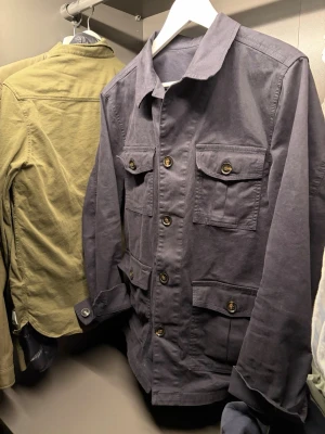 Mörkblå overshirt från Oscar Jacobson - Stilren mörkblå overshirt från Oscar Jacobson med fyra stora fickor framtill och klassisk krage. Endast använt ett fåtal gånger. Köptes ny på nk Gbg i höstas för 2500.