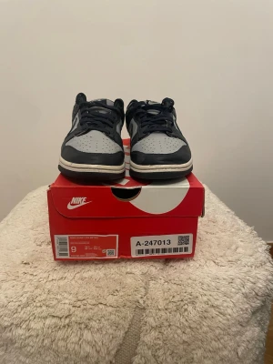 Nike Dunk Low Retro georgetown - Nike Dunk Low Retro sneakers i grått och marinblått läder med klassisk Swoosh på sidan. Lågt skaft, perforerad tå och vita sulor. Perfekta för dig som gillar streetwear och tidlös stil.