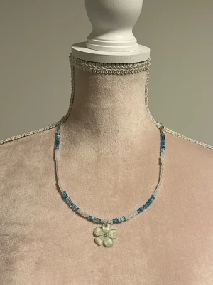 Blått pärlhalsband med blomma - NY! 💙 Sött halsband med med pärlor samt ett hänge i form av en blå blomma. Går att justera längden.  Köpt från en small business i USA (etsy). Säljer även den rosa versionen om man vill ha som bff halsband :3