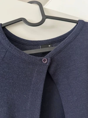 Mörkblå cardigan med knapp - Mörkblå cardigan med rund halsringning och en enkel knapp framtill. Långärmad och i mjukt, tunt material som passar perfekt till lager på lager. Enkel och stilren design som är lätt att matcha med olika outfits.