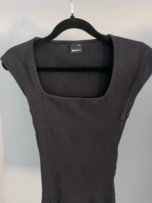 Svart ribbad topp från Gina Tricot - Snygg svart ribbad topp från Gina Tricot med fyrkantig ringning och korta ärmar. Toppen har en tight passform och är tillverkad i mjuk bomullsmix som känns skön mot huden. Perfekt att styla med jeans eller kjol för en trendig look.