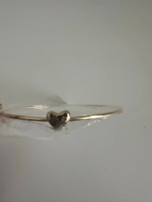 Guldfärgat armband med hjärta - Ett tunt, guldfärgat armband med en liten hjärtformad detalj framtill. Armbandet har en minimalistisk och stilren design som passar perfekt för dig som gillar enkla men snygga accessoarer. Helt NYTT!