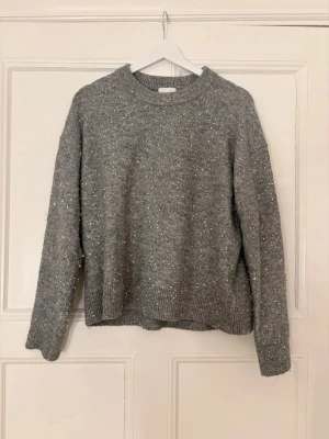 Grå stickad tröja - Den har små lösa trådar som kommer från paljetterna. Den e normal i storleken 