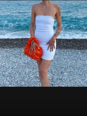 Vit axelbandslös kort klänning - Säljer en stilren vit axelbandslös kort klänning med tight passform. Klänningen har en enkel och clean design som framhäver siluetten. Perfekt för sommarens alla tillfällen och lätt att matcha med accessoarer.