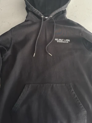 Helmut Lang hoodie  - Säljer en snygg svart Helmut Lang hoodie, skick; bra ända skavankerna är några sprickor i loggan på bröstet