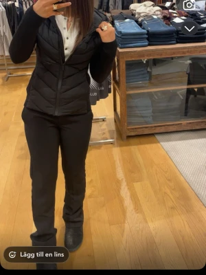 Svart pufferjacka med huva - Snygg svart pufferjacka med figurnära passform och huva. Jackan har dragkedja framtill och diskreta sömmar som ger en stilren look. Perfekt för kalla dagar och enkel att matcha med olika outfits. Materialet ser ut att vara syntet med lätt vaddering.