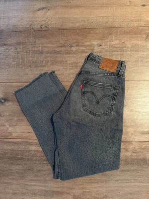 Grå Levi's vintage jeans 501  - Säljer ett par grå vintage Levi's jeans med klassisk femficksmodell och hög midja. Jeansen har raka ben och råa, avklippta benslut för en trendig look. Tillverkade i slitstark denim med den ikoniska röda Levi's-lappen på bakfickan. Cropped 