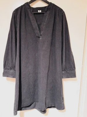 Svart/grå denimklänning från ARKET i strl 44 - Svart denimklänning i 100% bomull med vid ärm och avslappnad passform. Lätt A-linjeformad.  Storlek: 44 Bystvidd: 65 cm, omkrets ca 130 cm Material: 100% bomull Skick: Inga defekter eller fläckar, vissa naturliga skiftningar i tyget finns p.g.a denim-materialet från produktion & användning. Sparsamt använd. 