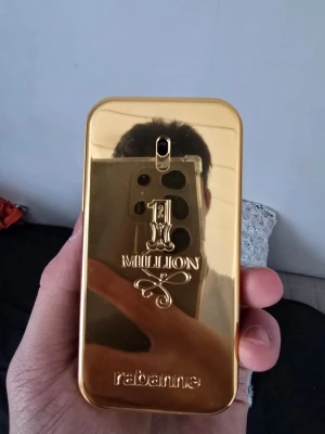 Paco Rabanne 1 Million Parfym 50/48ml - Säljer en ikonisk Paco Rabanne 1 Million parfym i en lyxig guldfärgad flaska med präglad logga och elegant svart detalj på sidan. Flaskan har en unik rektangulär form som påminner om en guldtacka och är tillverkad i metall och plast.