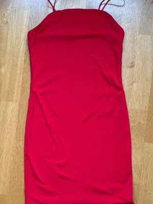 Röd kort klänning med tunna band - En enkel och snygg röd kort klänning med tunna axelband. Klänningen har en rak passform och ärmlös design, perfekt för varma dagar eller när du vill sticka ut. Materialet känns mjukt och följsamt mot kroppen. Små fläckar på klänningen, bifogad foton.