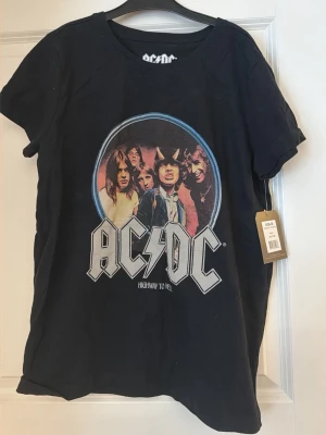 Svart AC/DC t-shirt med tryck - Cool svart t-shirt med stort AC/DC-tryck och motiv från 'Highway to Hell'. Rund halsringning och korta ärmar. Perfekt för dig som gillar bandtröjor och vill ha en avslappnad stil.