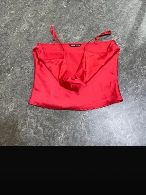 Röd satin linnetopp med tunna band - Snygg röd linnetopp i satin med tunna axelband och draperad urringning. Perfekt för dig som vill ha en trendig och stilren topp till sommaren. Materialet ger ett lyxigt intryck och toppen har en croppad passform.