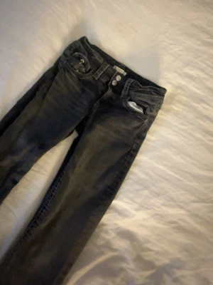 Svarta skinny jeans med dubbla knappar - Säljer ett par svarta utsvängda jeans med dubbla knappar i midjan och klassisk femficksdesign. Jeansen har en smal passform och är tillverkade i stretchigt denimtyg för extra komfort. Perfekta till en avslappnad eller trendig look. 