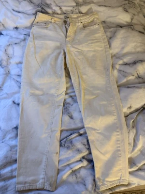 Vita raka jeans - Säljer ett par vita jeans med rak passform och hög midja. Klassisk femficksmodell med knapp och dragkedja framtill. Perfekta att styla med en crop top eller hoodie för en clean look.