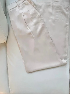 Crèmefärgad kostymbyxa från Beaumont - Stilrena satinbyxor i créme/guldskimrande tyg från Beaumont i rak modell. Byxorna har pressveck och diskreta fickor, vilket ger en clean och klassisk look. Materialet har en lätt glansig finish som känns lyxig och passar perfekt till en dressad outfit. Storlek 36 på lappen men motsvarar en 38 till måtten: