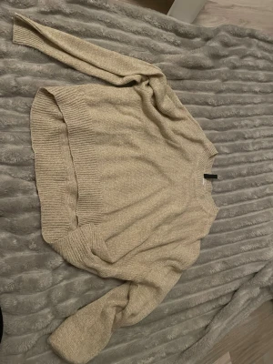 Beige stickad tröja från H&M Divided - Snygg beige stickad tröja från H&M Divided. Tröjan har en avslappnad passform med breda ribbstickade muddar vid ärmslut och nederkant. Perfekt för lager-på-lager och enkel att matcha med jeans eller kjol. Kortare variant 