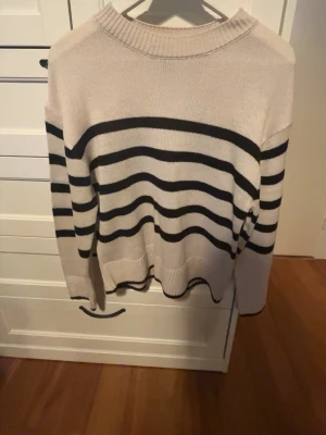 Randig stickad tröja från h&m - Säljer en beige stickad tröja från Divided med svarta horisontella ränder. Tröjan har rund halsringning och långa ärmar. Perfekt för dig som gillar klassisk och enkel stil med en twist av marint. Skulle säga att tröjan är mer som storleken S.