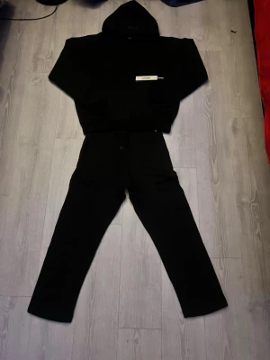 🖤 Essentials Fear of God – Svart (M) / Komplett set - 🔥 Essentials Fear of God – Svart hoodie + byxor (M) Stilrent, mörkt och riktigt clean Essentials-set i svart. Hoodien har den klassiska ESSENTIALS-texten framtill, och byxorna matchar perfekt. Passformen är oversized-inspirerad, mjuk och skön — perfekt för vardag, streetwear eller chill-outfits. Fint skick och redo att användas! 🖤✨ 💬 Bud välkomnas – pris kan diskuteras! 📦 Skickas direkt! 🧵 Material: bomullsblandning 🎨 Färg: svart 📏 Storlek: M 👕 Set: hoodie + joggers 🌟 Passform: relaxed / essenti