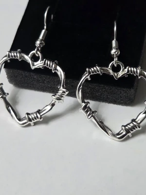 Taggtrådshjärtan – Örhängen i Rostfritt Stål - Riktigt unika örhängen formade som hjärtan i taggtrådsstil. De ger en snygg "edgy" känsla till vilken outfit som helst och är tillverkade i rostfritt stål, vilket gör att de håller sin glans och är skonsamma mot öronen. ​Helt nya och aldrig använda! ​Detaljer: ​Material: Rostfritt stål ​Färg: Silver ​Mått: Ca 2.5 cm 