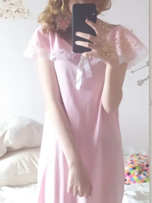 Rosa nattlinne med spets och rosetter på framsidan och sidorna - Sött rosa nattlinne. Framtill sitter en dekorativ vit rosett och på sidorna sitter det också rosetter. Nattlinnet har en lös och bekväm passform.