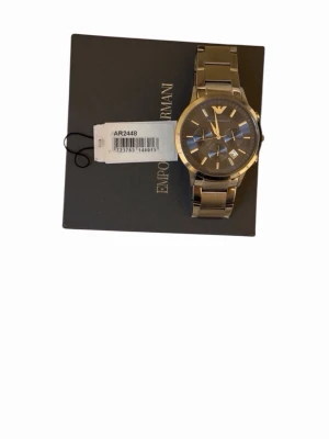 Emporio Armani silverfärgad klocka - Stilren klocka från Emporio Armani i silverfärgat metallarmband och rund urtavla. Klockan har markerade index, tre mindre urtavlor och klassisk logga vid tolvslaget. Perfekt accessoar för dig som gillar en clean och modern look.